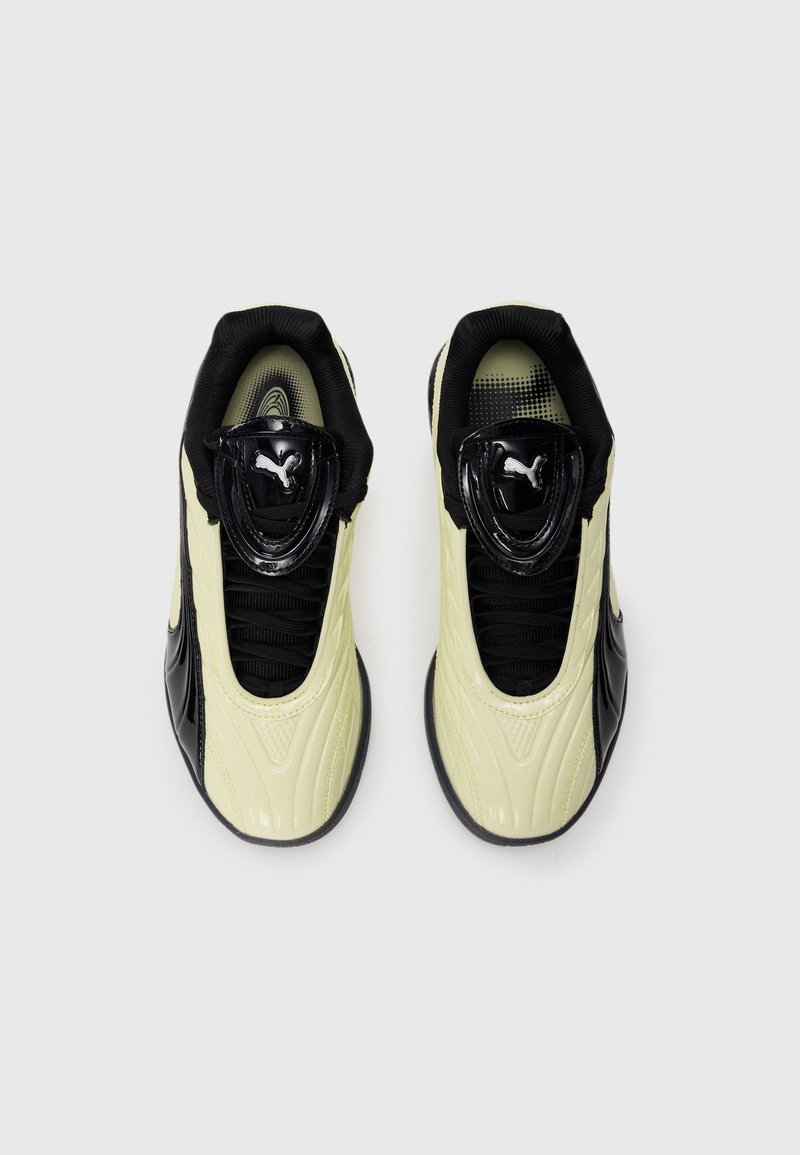 Des baskets noires et jaune clair présentent une surface brillante et texturée, un design de lacets élastiques, et un col rembourré pour le confort.