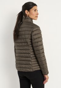 Olivgrön pufferjacka med hög krage, horisontell sömnad och en lätt, glänsande textur. Fitted design, sömnadsdetaljer synliga.