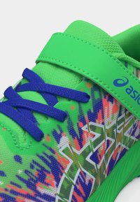 Φωτεινό πράσινο αθλητικό παπούτσι ASICS με μπλε κορδόνια, λουράκι με βέλκρο και πολύχρωμα αφηρημένα σχέδια στην πλευρική επιφάνεια.