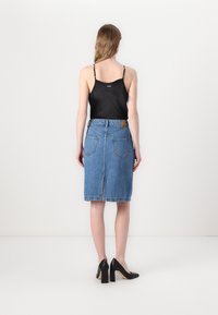 Camisola nera in satin con spalline sottili abbinata a una gonna midi in denim blu con due tasche posteriori e orlo grezzo. Scarpe con tacco alto nere.