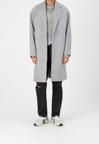 Grå ullkappa med avslappnad passform, kammat slag och två knappar. Bärs över en ribbad tröja och kombineras med svarta rivna jeans och sneakers.