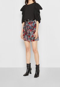 Top nero con maniche a sbuffo e cintura, abbinato a una gonna a fantasia floreale nei colori rosso, blu e grigio. Stivaletti neri alla caviglia completano l'outfit.