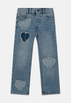 Jean en denim bleu clair avec quatre patchs en forme de cœur effilochés de différentes nuances de bleu sur les jambes avant, bouton et passants de ceinture visibles.