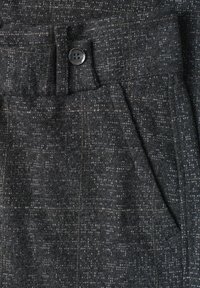 Tissu texturé gris foncé avec une poche à rabat boutonnée et une poche latérale inclinée sur un vêtement, montrant le détail du tissage.