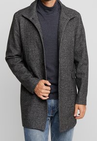 Abrigo gris de mezcla de lana con acabado texturizado, cierre de botones, cuello con muesca, bolsillos laterales y un ajuste ligeramente relajado, combinado con un suéter de cuello alto a rayas.