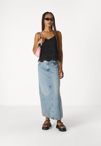 Top court en dentelle noire avec un ourlet festonné, jupe en denim bleu clair taille haute, sandales à plateforme noires et petit sac à main rose.