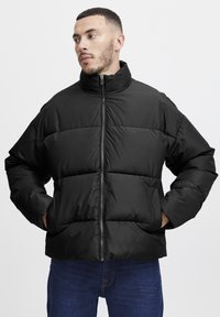 Black puffer jacket with a stand-up collar, zip closure, and horizontal stitching. Features side pockets and a relaxed fit. Textured fabric.