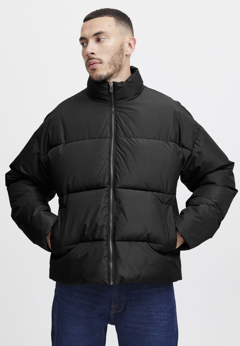 Black puffer jacket with a stand-up collar, zip closure, and horizontal stitching. Features side pockets and a relaxed fit. Textured fabric.
