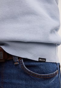 Suéter de punto azul claro con dobladillo acanalado, combinado con jeans de mezclilla azul oscuro. Etiqueta "BIG STAR" visible en el dobladillo del suéter.