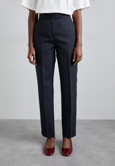 Pantalons gris foncé sur mesure à taille haute, dotés de plis sur le devant et d'une coupe droite. Associés à des ballerines rouges brillantes.