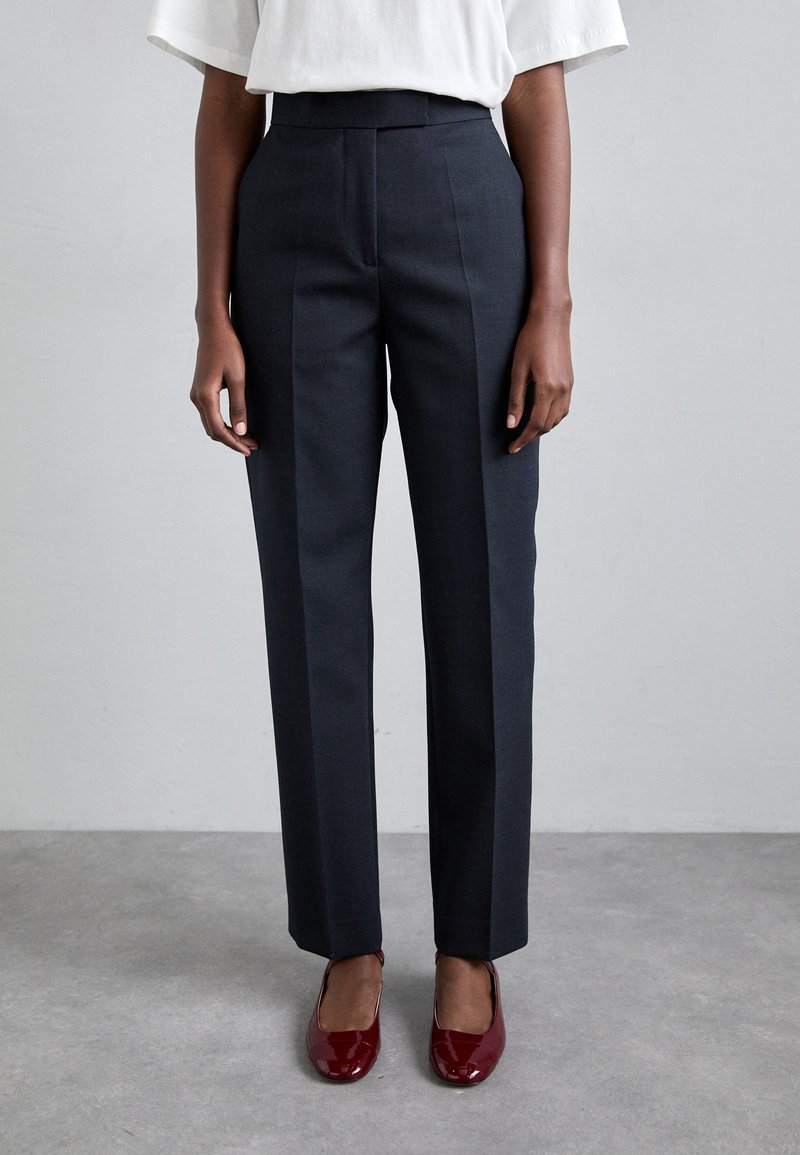 Pantaloni personalizați de culoare gri închis, cu talie înaltă, având pliseuri frontale și un design drept. Asortați cu balerini lucioși roșii.