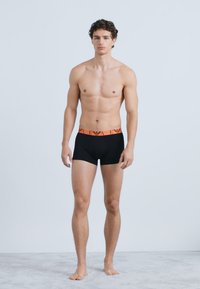 Boxer neri con fascia elastica arancione con un logo. Il capo presenta un design aderente e una texture del tessuto liscia.