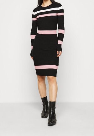 Femme portant une robe noire mi-longue aux genoux avec des rayures horizontales roses et blanches et des bottines noires.