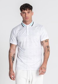 Biely polo tričko s jemným geometrickým vzorom po celom povrchu, kontrastným pruhovaným golierom a krátkymi rukávmi. Vyrobené z mäkkej, priedušnej tkaniny.