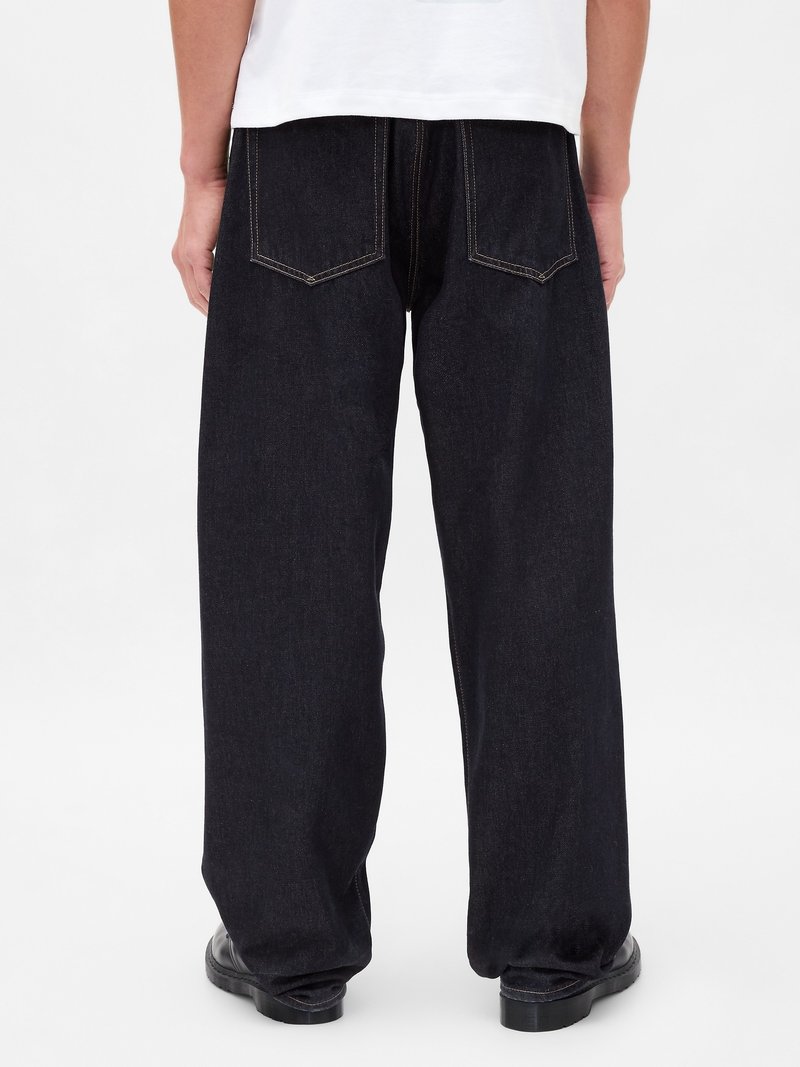 Voľné tmavé džínsy so strihom rovného nohavice, s zadnými vreckami a viditeľným žltým stehom. Materiál sa zdá byť odolný denim.