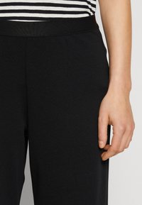 Czarne elastyczne spodnie mają gładką, miękką teksturę i elastyczny pas. Pasiasta koszulka jest częściowo widoczna nad pasem.