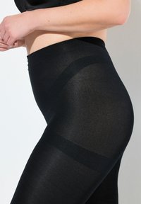 Leggings neri realizzati in un materiale liscio e elasticizzato, con una vita alta e un leggero lucido, caratterizzati da un design aderente sui fianchi e sulle cosce.