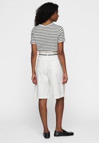 Witte linnen shorts met twee achterzakken, gecombineerd met een zwart-wit gestreept cropped t-shirt. De outfit heeft een riem en platte schoenen.