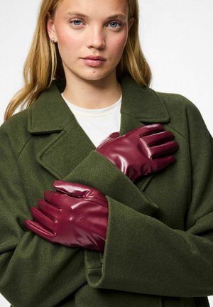 Guantes de cuero burdeos con textura suave, con diseño de cinco dedos, llevados con las manos entrelazadas sobre un abrigo verde.