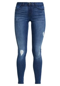Jeans ajustados de denim azul oscuro, con un lavado desgastado, parches de desgaste notorios y un diseño clásico de cinco bolsillos.