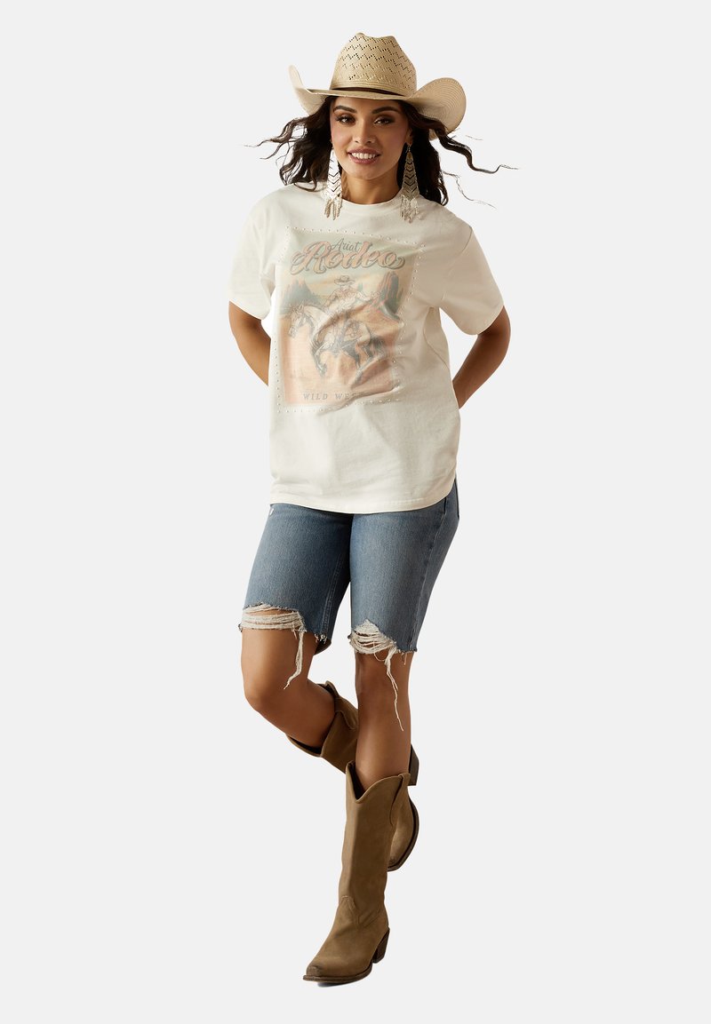 White short-sleeve t-shirt with rodeo graphic, paired with distressed denim shorts and brown cowboy boots. Cowboy hat and earrings complete the look.