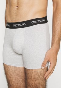 Graue Baumwollboxershorts mit einem schwarzen Bund, auf dem der Text "ONLY&SONS" in Weiß steht. Der Stoff ist glatt und eng anliegend.