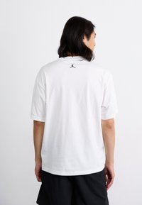 Hvit koks-årmet t-skjorte laget av bomull med rund hals. Har en liten svart Jumpman-logo øverst på ryggen.