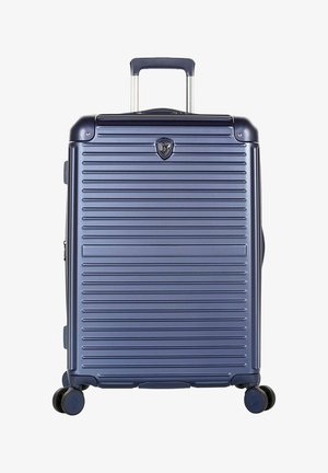 Valise rigide bleu marine avec des rainures horizontales, quatre roues et une poignée télescopique noire étendue.