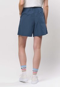 Laivastonsiniset shortsit, joissa on joustava vyötärönauha, sivutaskut ja takatasku. Yhdistetty valkoisiin tennareihin ja monivärisiin raidallisiin sukkiin.