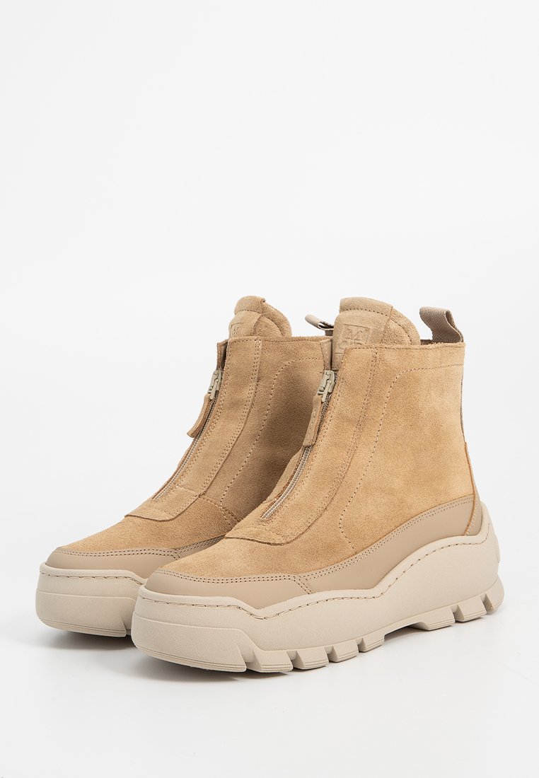Botas de tobillo de ante color beige con una suela de goma gruesa color crema, que cuentan con dos cremalleras laterales y una punta redondeada, acentuadas por un diseño de estilo senderista.