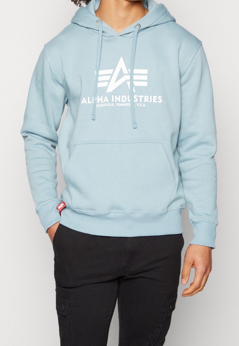 Felpa con cappuccio azzurro chiaro con una tasca frontale, caratterizzata da un logo bianco e testo. Realizzata in materiale morbido, ha un cappuccio con coulisse e polsini a coste.