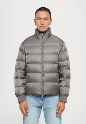 Siva puffer jakna s visokim kragnom, s sjajnom završnom obradom i dijagonalnim uzorkom. Rebrasti manžeti za udobno pristajanje.