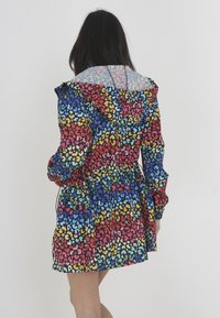 Veste légère multicolore avec un motif de léopard vibrant, dotée d'une capuche transparente et d'une taille froncée.