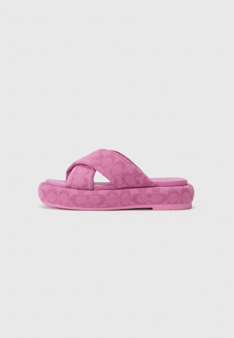 Rosa Plattform-Sandale mit Kreuzband, dekoriert mit einem dezenten kreisförmigen Muster auf den Riemen und der Sohle, vor einem schlichten weißen Hintergrund.