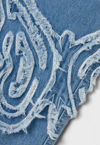 Přeplátovaný denimový materiál s jemným modrým vzorem, s intricními texturami a nepravidelným okrajem.