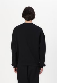 Sort sweatshirt med en afslappet pasform, lange ærmer, ribbet krave og manchetter, lavet af blødt stof. Bagsiden har ingen særligt bemærkelsesværdige mønstre eller detaljer.
