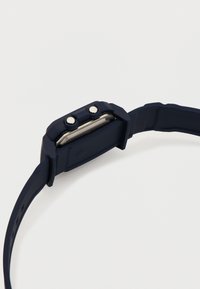 Ψηφιακό ρολόι με λουρί από καουτσούκ σκούρου μπλε χρώματος, δύο ασημένια πλευρικά κουμπιά και ορθογώνια μεταλλική θήκη, τοποθετημένο σε λευκό φόντο.