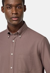 Camicia button-up beige chiaro con una piccola tasca sul petto, realizzata in tessuto testurizzato; presenta un colletto classico e bottoni bianchi.