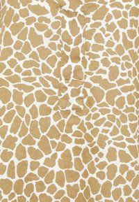 Tecido com padrão de girafa com formas irregulares em tons de castanho sobre um fundo creme. O material apresenta uma textura com um leve padrão de trançado. Inclui uma pala central.