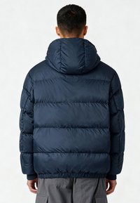 Giacca imbottita blu navy con cappuccio, caratterizzata da un design trapuntato, polsini elastici e fondo arricciato, realizzata in materiale liscio e leggero.