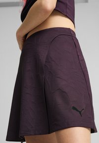 Shorts de sport violets en tissu texturé. Ils comportent des coutures latérales et un petit logo noir à l'ourlet. Coupe taille moyenne.