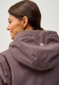 Chaqueta con capucha para mujer en un tono mauve suave. Tejido ligero y suave con un brillo sutil. Presenta un detalle bordado de copo de nieve en la parte posterior.