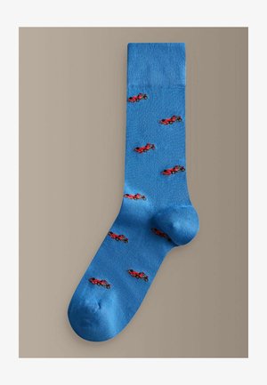 Niebieska skarpetka z małymi czerwonymi wzorami wyścigowych samochodów równomiernie rozmieszczonymi na materiale, przedstawiona na neutralnym tle.