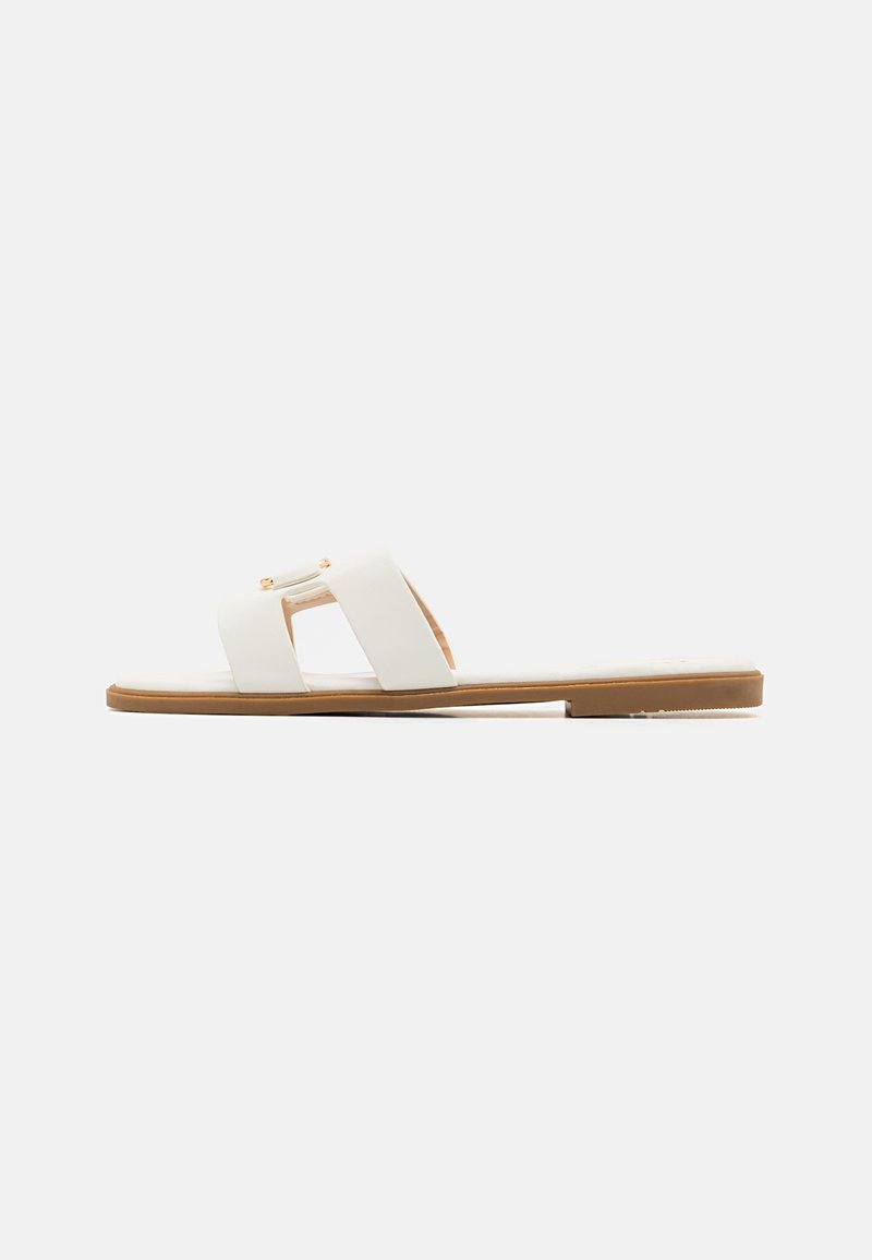Flat white slide sandal with two wide straps and a tan sole, shown from the side on a plain light background.