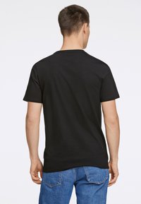 Musta puuvillapaita, jossa on pyöreä kaula-aukko ja lyhyet hihat, yhdistettynä sinisiin farkkuihin, kuvattu takaa. Sileä rakenne.