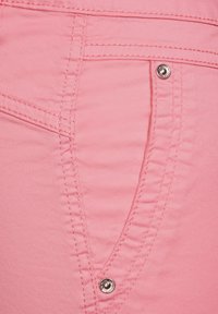 Tessuto rosa chiaro con un primo piano di una tasca con cuciture a contrasto e un dettaglio in metallo argentato. Superficie texturizzata con finitura liscia.