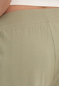 Olijfgroene geribde broek met een brede elastische tailleband en textuurstof, met plooien die een subtiele detail aan het ontwerp toevoegen.