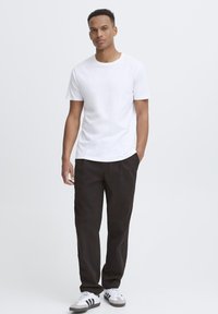 Maglietta bianca in cotone e pantaloni neri. La maglietta ha un collo tondo e maniche corte. Completata con scarpe da ginnastica bianche e grigie.