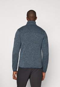 Men's blue, textured fleece jacket with a high collar and full sleeves, featuring a zippered back pocket and subtle stitch details.