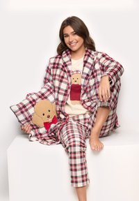 Plaid pajama set in red and white, featuring a teddy bear design on the shirt. Includes a matching robe and decorative pillow with bear.